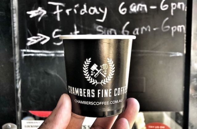 Holding a cup of coffee in front of the trading hours of Chambers Fine Coffee