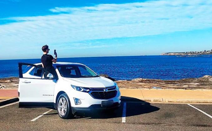 James Banham standing in a Holden Equinox SUV car to take a picture of the ocean