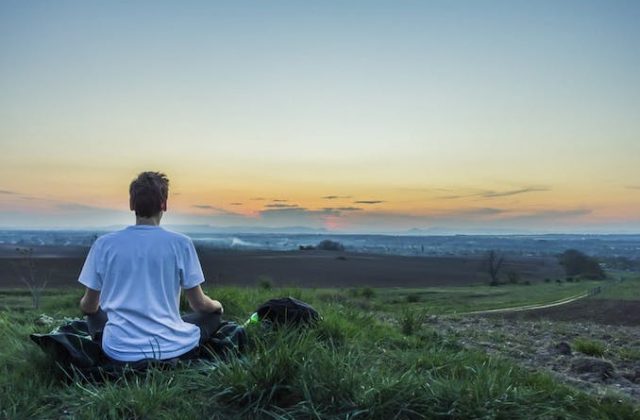 Man doing yoga on a hill overlooking a town