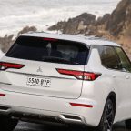 A Mitsubishi outlander drives away from the camera along a coastal road